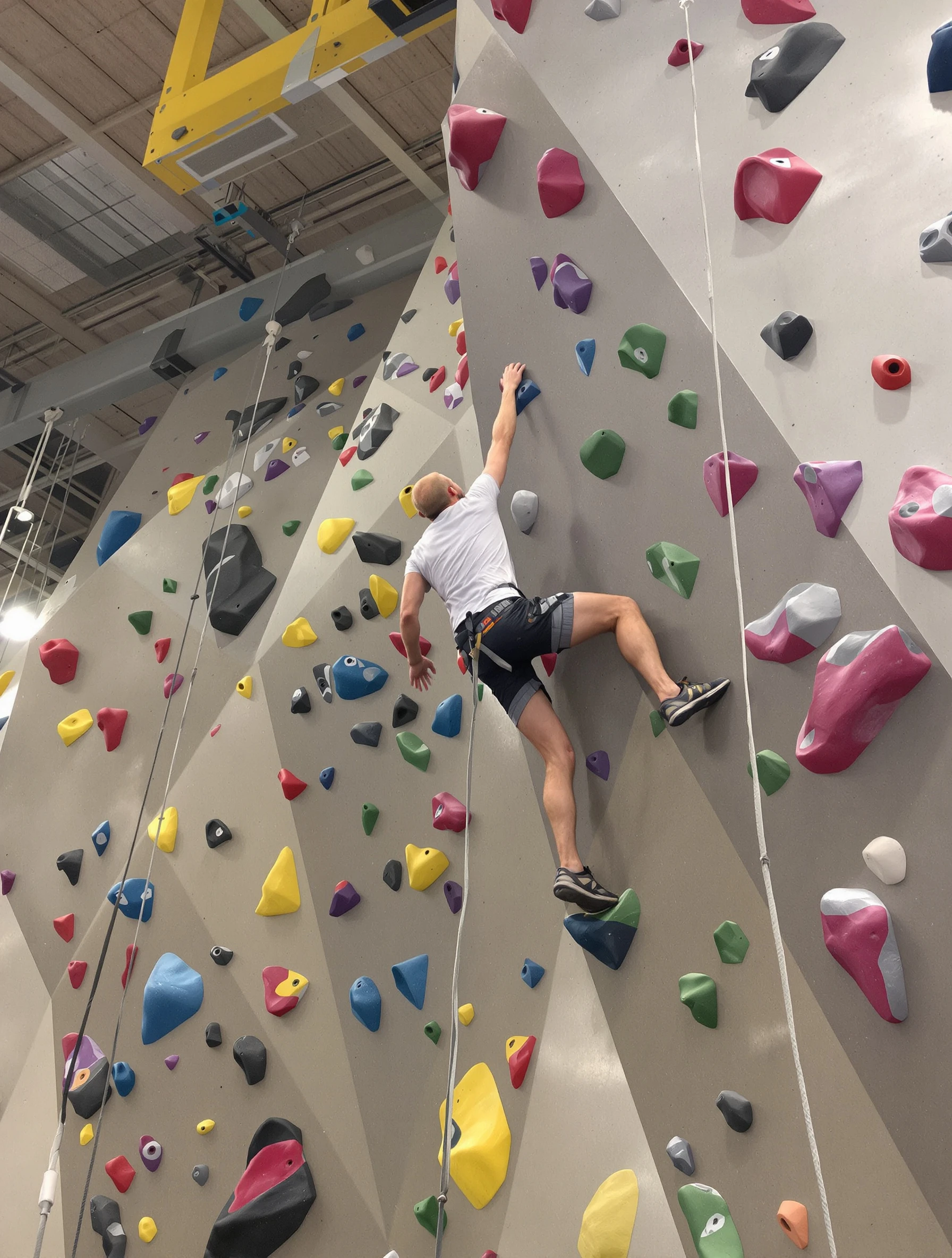 Man climbing challenging indoor rock wall, reaching for next hold. Climbing shoes and chalk, colorful holds, problem-solving strength.