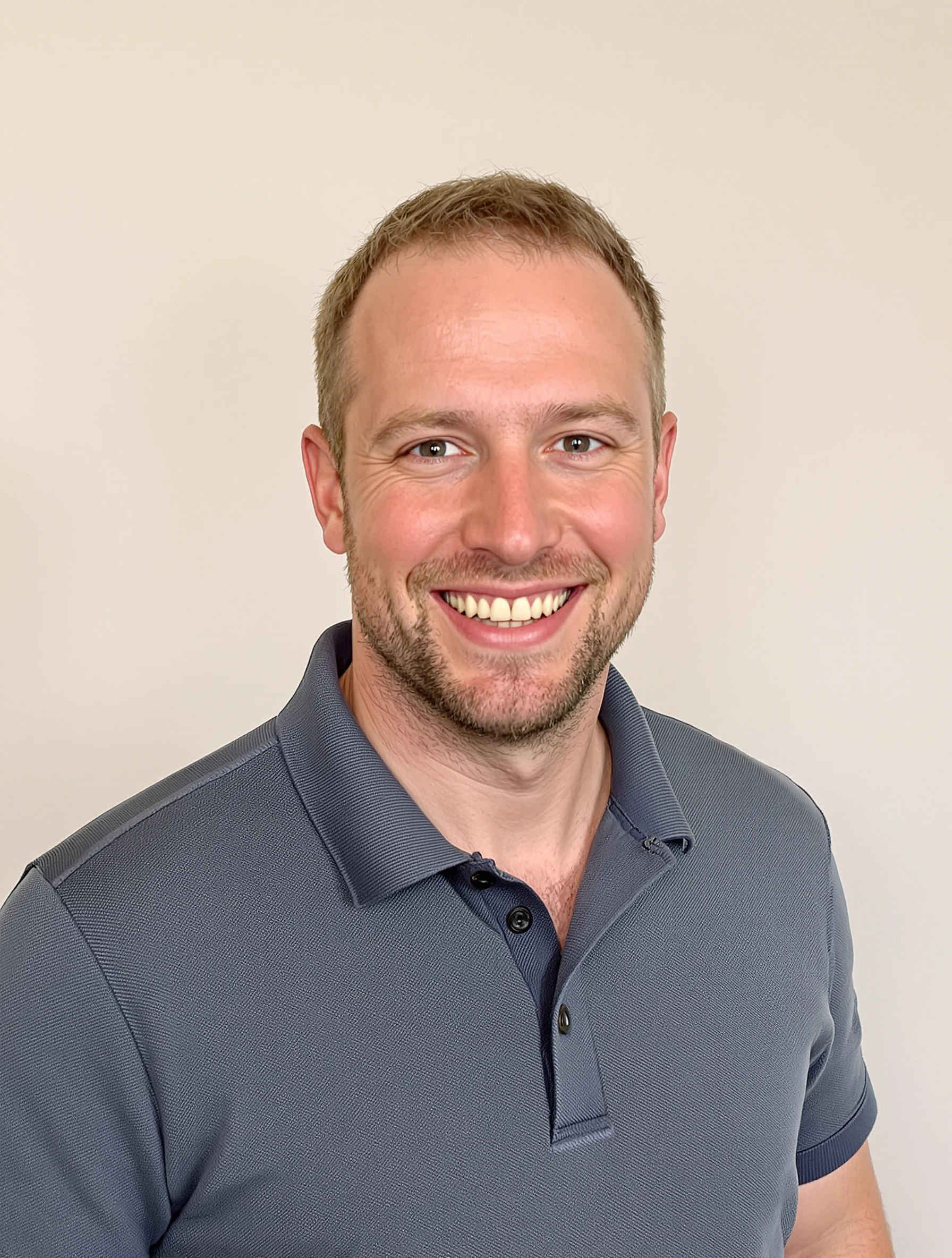 Headshot of a man in a slate blue knit polo shirt, neutral backdrop, friendly smile, smart-casual startup look.