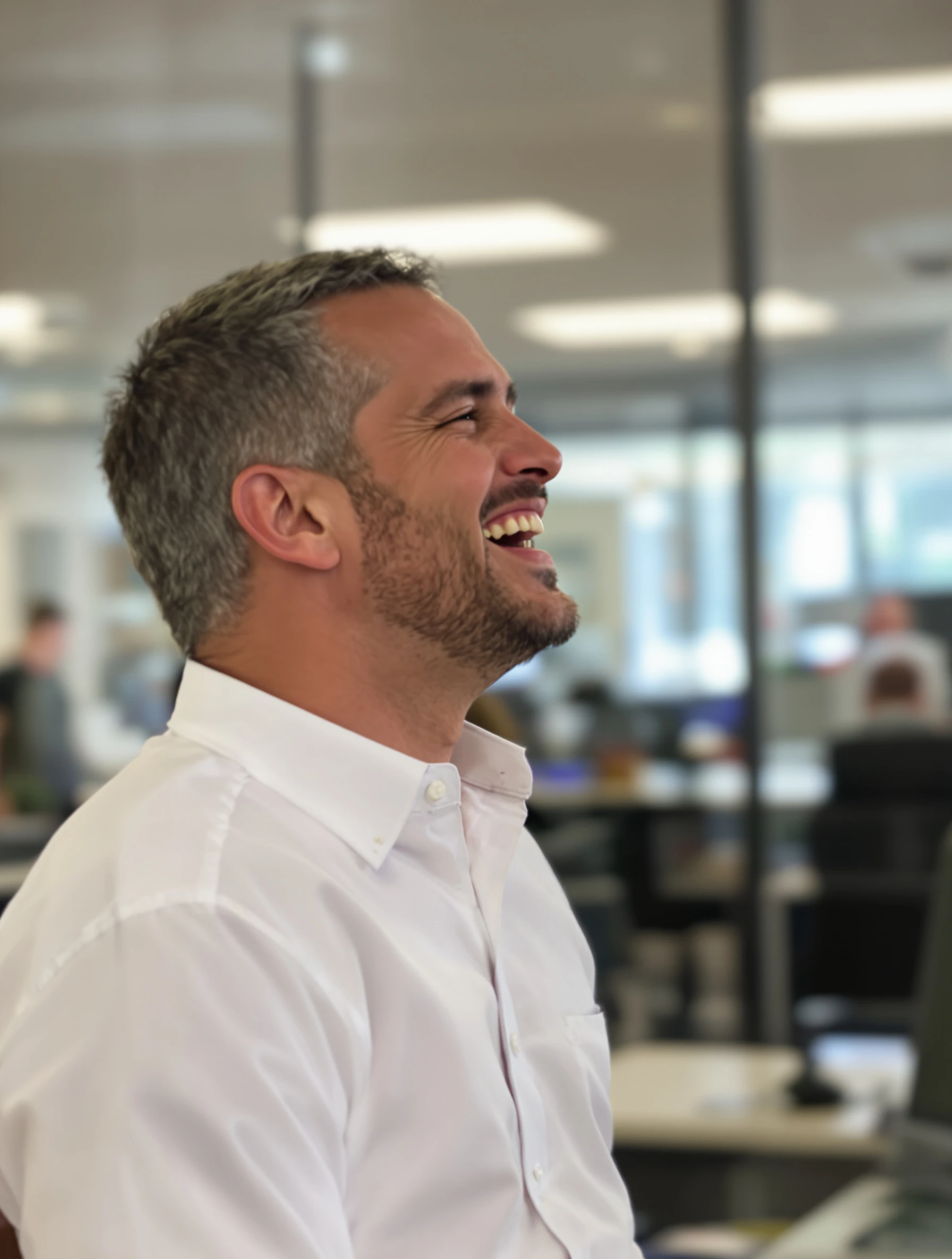 Candid-style headshot of a man mid-laugh, head slightly tilted, white shirt with sleeves rolled, bright office blurred behind him.