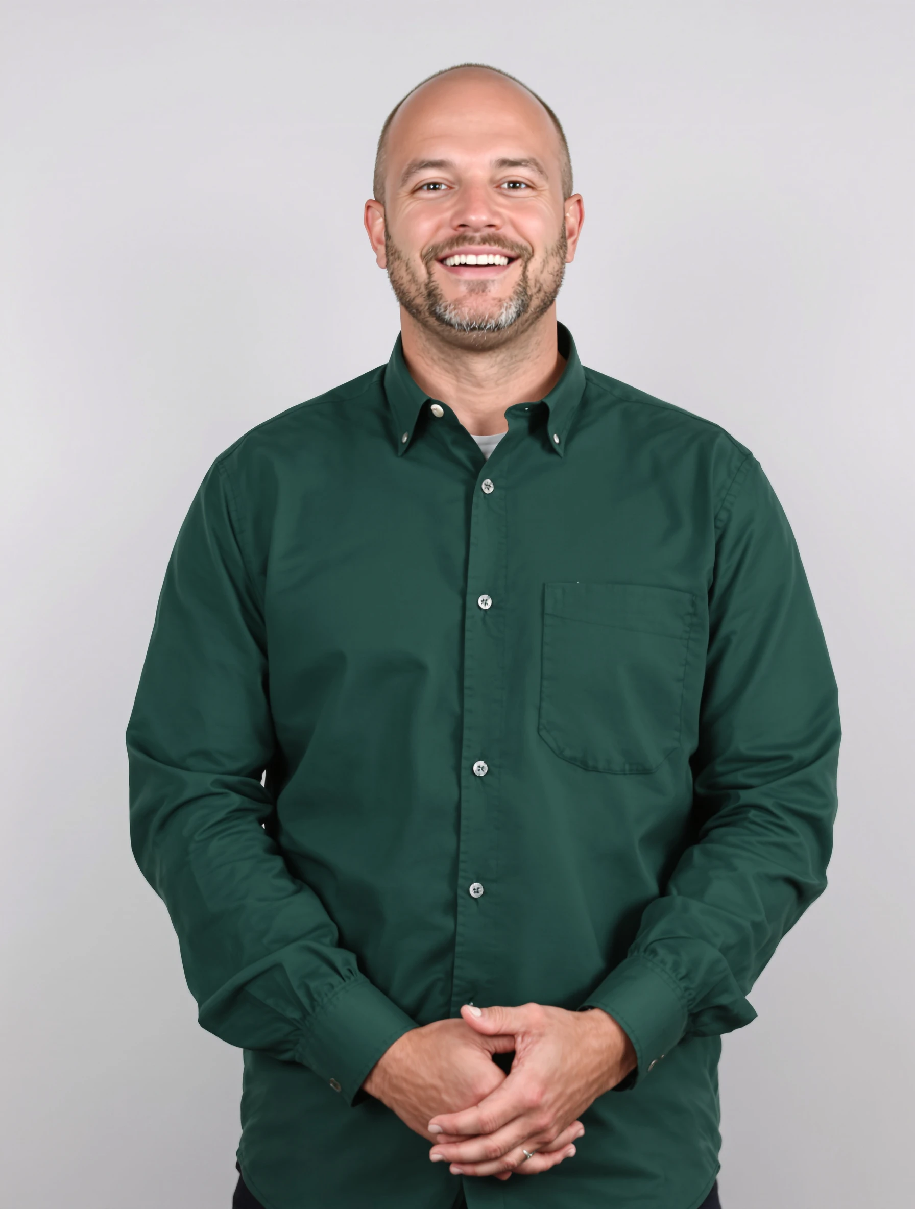 Headshot of a man straight on to the camera, square shoulders, forest green shirt, hands clasped in front, light grey backdrop, warm approachable smile.
