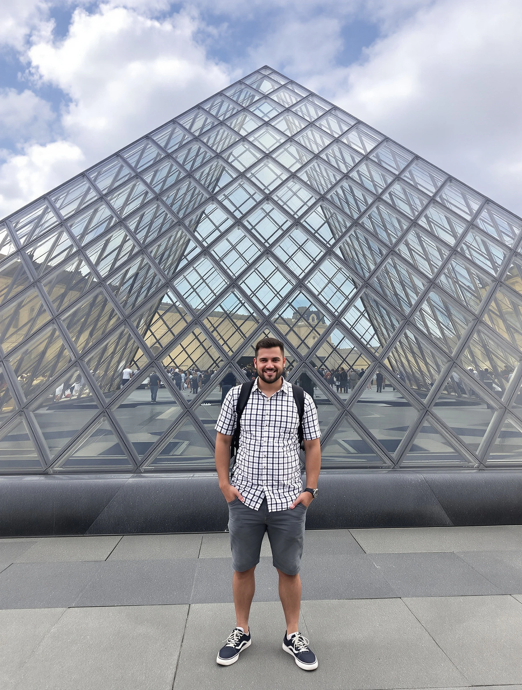 Man at the Louvre pyramid, smart casual tourist attire. Iconic glass pyramid entrance, architectural appreciation, cultu